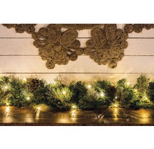 Decoratieve scène met jute krans, dennen groen, kegels en lichtslingers op een houten tafel voor een houten muur.