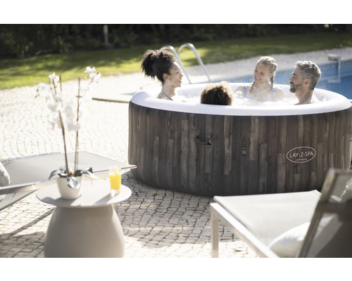 Opblaasbare jacuzzi met houten bekleding in de tuin met ontspannende mensen.