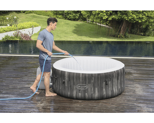 Man vult een opblaasbare whirlpool met water in de tuin.