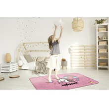 Een meisje springt op een rechthoekig, roze vloerkleed met eenhoornmotief in een kinderkamer.