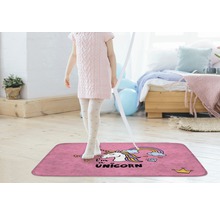 Meisje staat op een roze tapijt met eenhoornmotief in een lichte kamer.