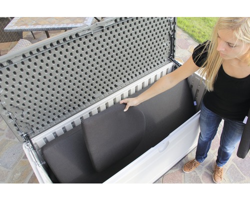 Vrouw ruimt kussens op in een grijze en witte tuinkist.