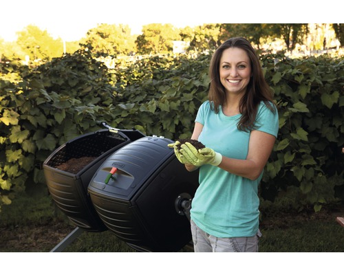 Vrouw houdt aarde vast voor een roterende compostbak in de tuin.