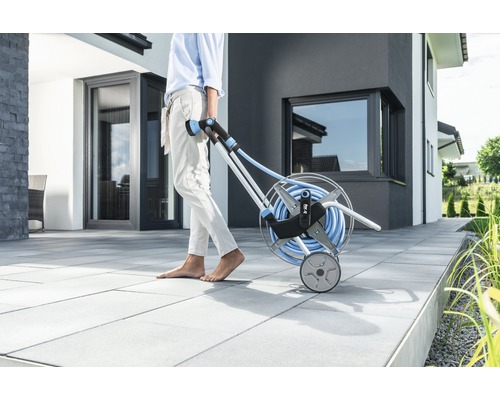 Tuinscene met persoon die een slangwagen met tuinslang trekt.