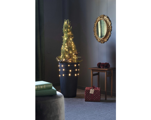 Gedecoreerde miniatuurkerstboom in een pot met cadeaus in een kamer