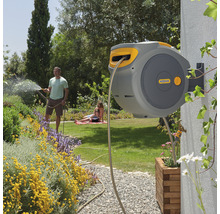 Automatische slangbox aan een huismuur met een man die de tuin besproeit