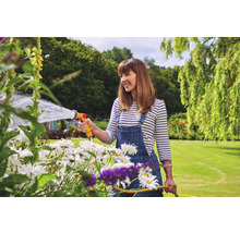 Vrouw besproeit bloemen in de tuin met een tuinslang.