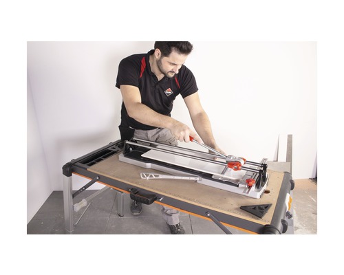 Een man gebruikt een tegelsnijmachine op een werktafel om tegels te snijden.