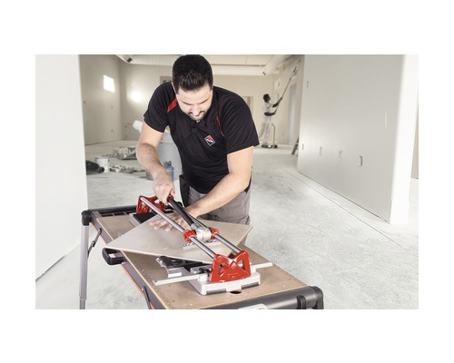 Een man snijdt tegels met een tegelsnijder in een gerenoveerde ruimte.