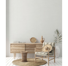 Lichte woonkamer met houten dressoir, fauteuil, strohoed en decoraties op een rond vloerkleed.