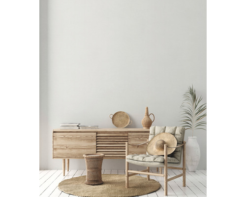 Lichte woonkamer met houten dressoir, fauteuil, strohoed en decoraties op een rond vloerkleed.