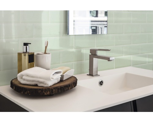 Badkamer met wastafel, kraan, handdoeken en groene tegels