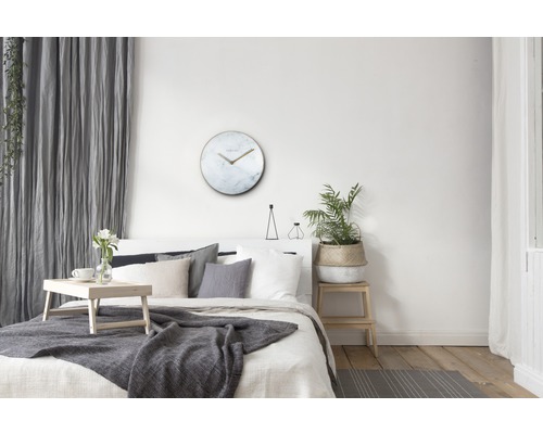Lichte slaapkamer met bed, tafel, plant en ronde wandklok