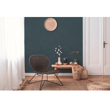 Woonkamer met rotan stoel, houten tafel, vazen, jute tapijt en decoratie voor een donkergroene muur