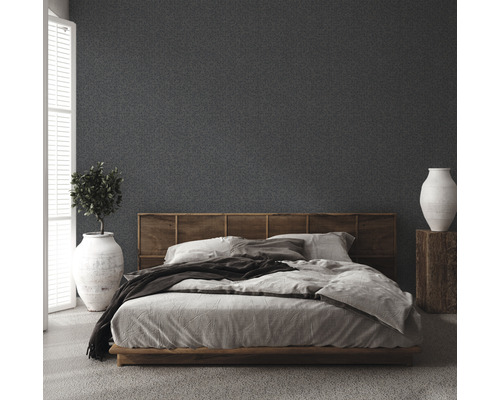 Slaapkamer met bed, houten hoofdeinde, plant in pot en vaas op een houten sokkel voor een gestructureerde muur