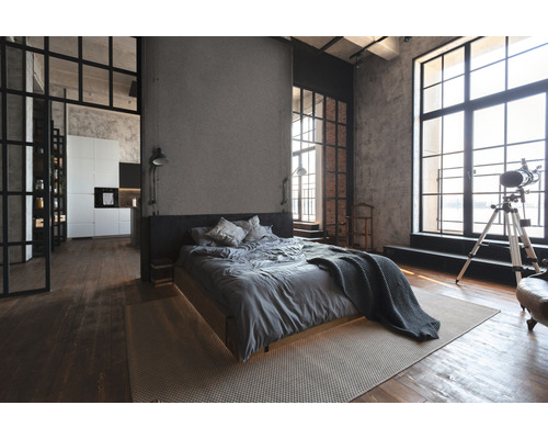 Interieurfoto van een slaapkamer in loftstijl met bed, ramen en houten vloer.