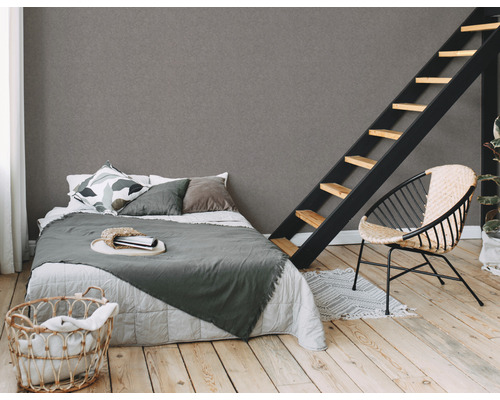 Slaapkamer met bed, ladder en rotan stoel op een lichte houten vloer tegen een grijze muur