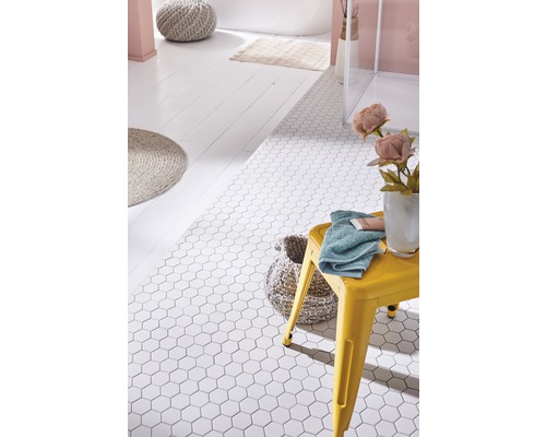 Badkamer met witte, zeshoekige vloertegels, gele kruk, handdoek en badkameraccessoires.