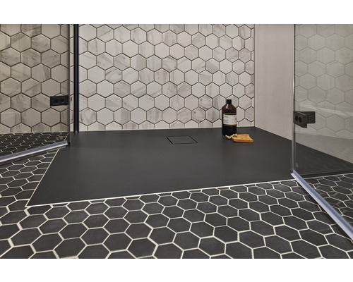Gelijkvloerse douche met zwart douchegedeelte en zeshoekige tegels op de wand en vloer.