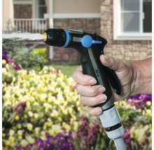 Een hand houdt een tuinspuit vast en geeft planten water.