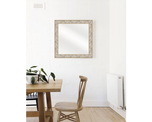 Decoratieve spiegel met houten frame boven een eettafel aan een muur.