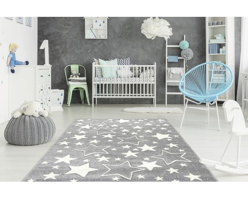 Kinderkamer met grijs tapijt met witte sterren, babybed, commode en speelgoed.