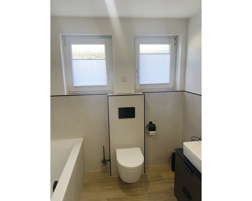 Lichte badkamer met toilet, wastafel, bad en twee ramen met plisségordijnen