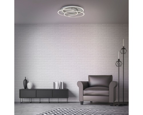 Woonkamer met plafondlamp, fauteuil en decoratie op een dressoir voor een bakstenen muur