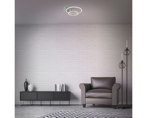 Woonkamer met plafondlamp, fauteuil en dressoir voor een bakstenen muur.