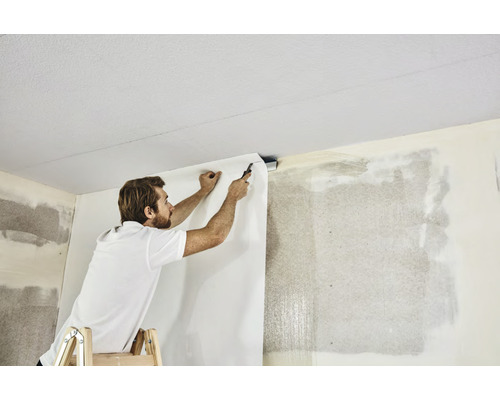 Een man op een ladder brengt behang aan op de muur