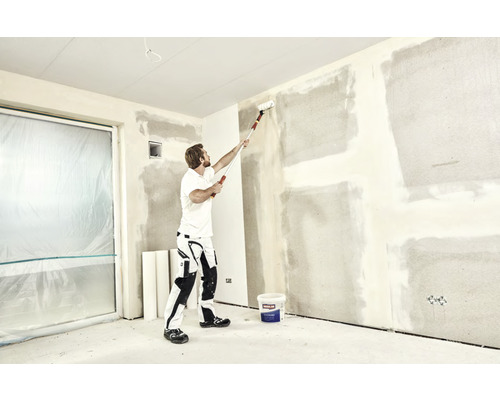 Een man gebruikt een verfroller op een muur in een kamer die wordt gerenoveerd.