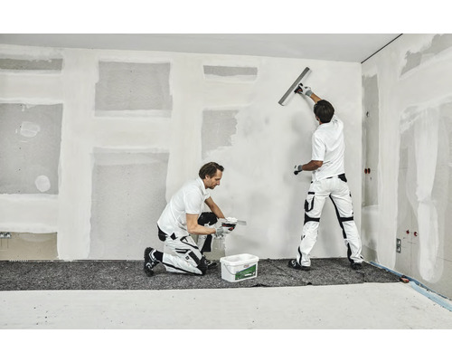 Twee vakmensen pleisteren een muur in een kamer.