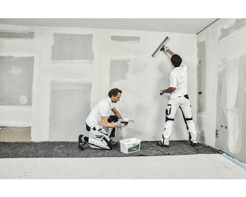 Twee vakmensen plamuren een muur in een interieur.