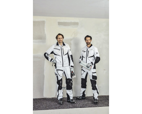 Twee vakmensen in werkkleding voor een muur binnenshuis.