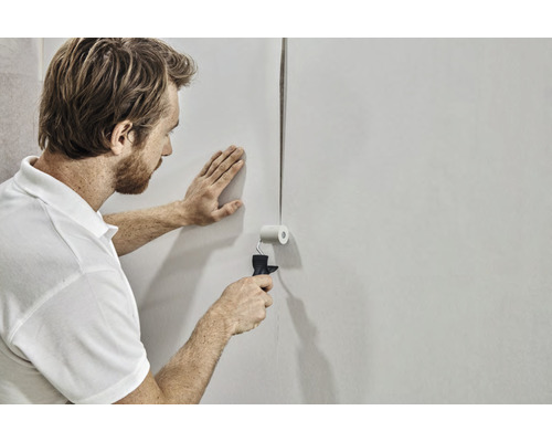 Man plakt behang met een aandrukroller op de muur