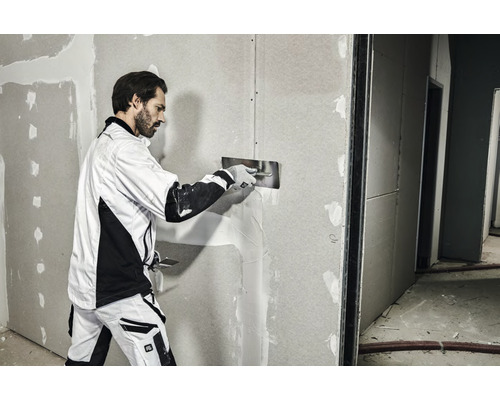 Een man plamuurt een gipsplatenwand met een plamuurmes.