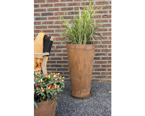 Hoge plantenpot met beplanting in de tuin voor een bakstenen muur