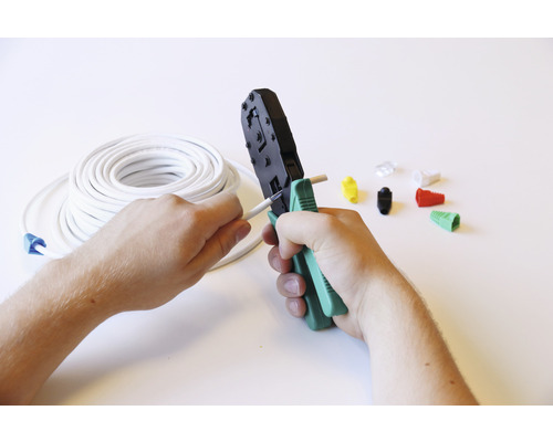 Een netwerkkabel wordt bewerkt met een krimptang, op de achtergrond een kabelhaspel en netwerkstekkers.