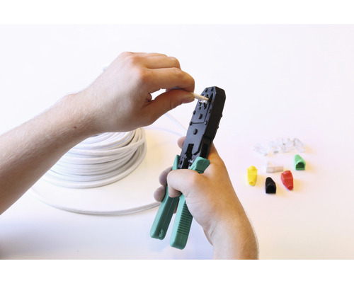Een man gebruikt een krimptang om een kabel te bewerken. Op de achtergrond bevinden zich een rol kabel en stekkers.