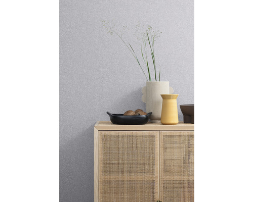 Behang met patroon boven een kast met rotan voorkant, met daarop vazen en een schaal