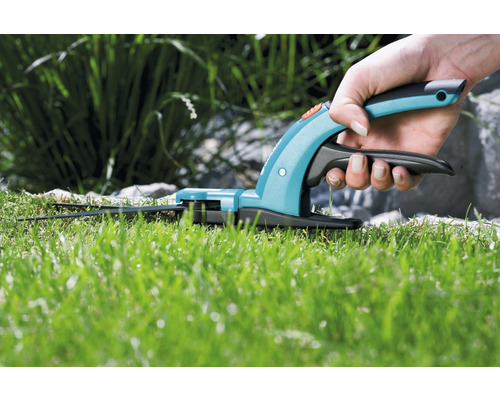 Een hand houdt een grasschaar boven een gazon.