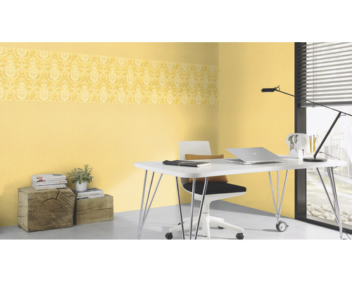 Kantoor met geel, gedessineerd behang met sierrand, bureau, stoel en accessoires.
