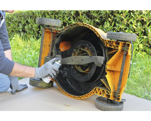 Een persoon spuit roestbescherming op een omgekeerd gazonmaaierdek.