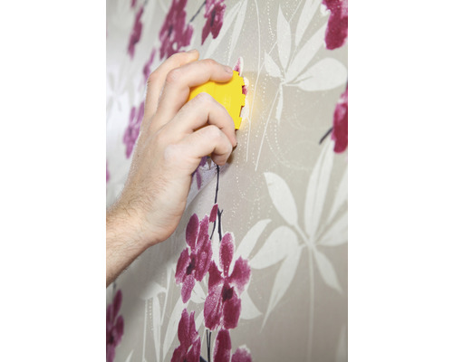 Hand met behangafsteker verwijdert bloemenbehang