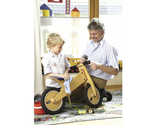 Een man monteert met een kind een houten loopfiets in een kinderkamer.