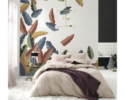 Slaapkamer met bed voor een wand met tropische bladeren, een lamp en een badkamer met ligbad.