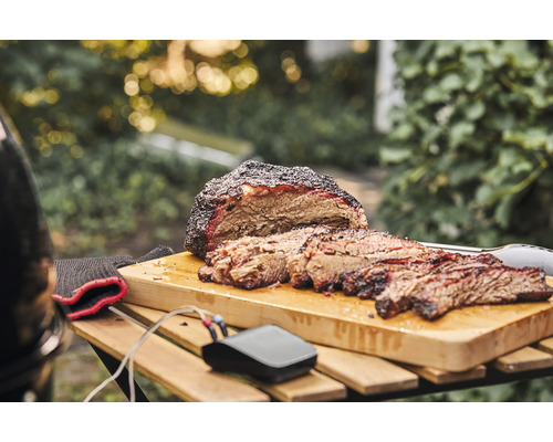 Gesneden brisket op een snijplank met thermometer en barbecuegereedschap