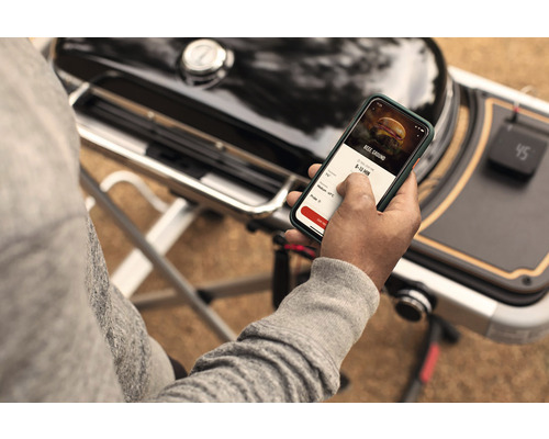 Persoon gebruikt een app op een smartphone naast een barbecue.