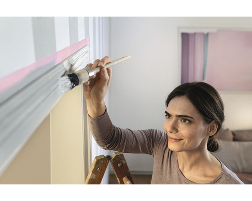 Vrouw schildert een muur met een kwast en verf.