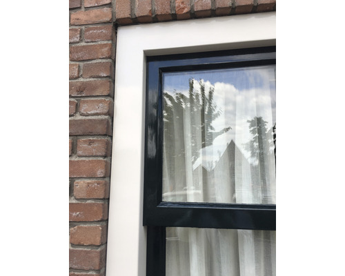 Close-up van een raam met kozijn en uitzicht op een bakstenen muur